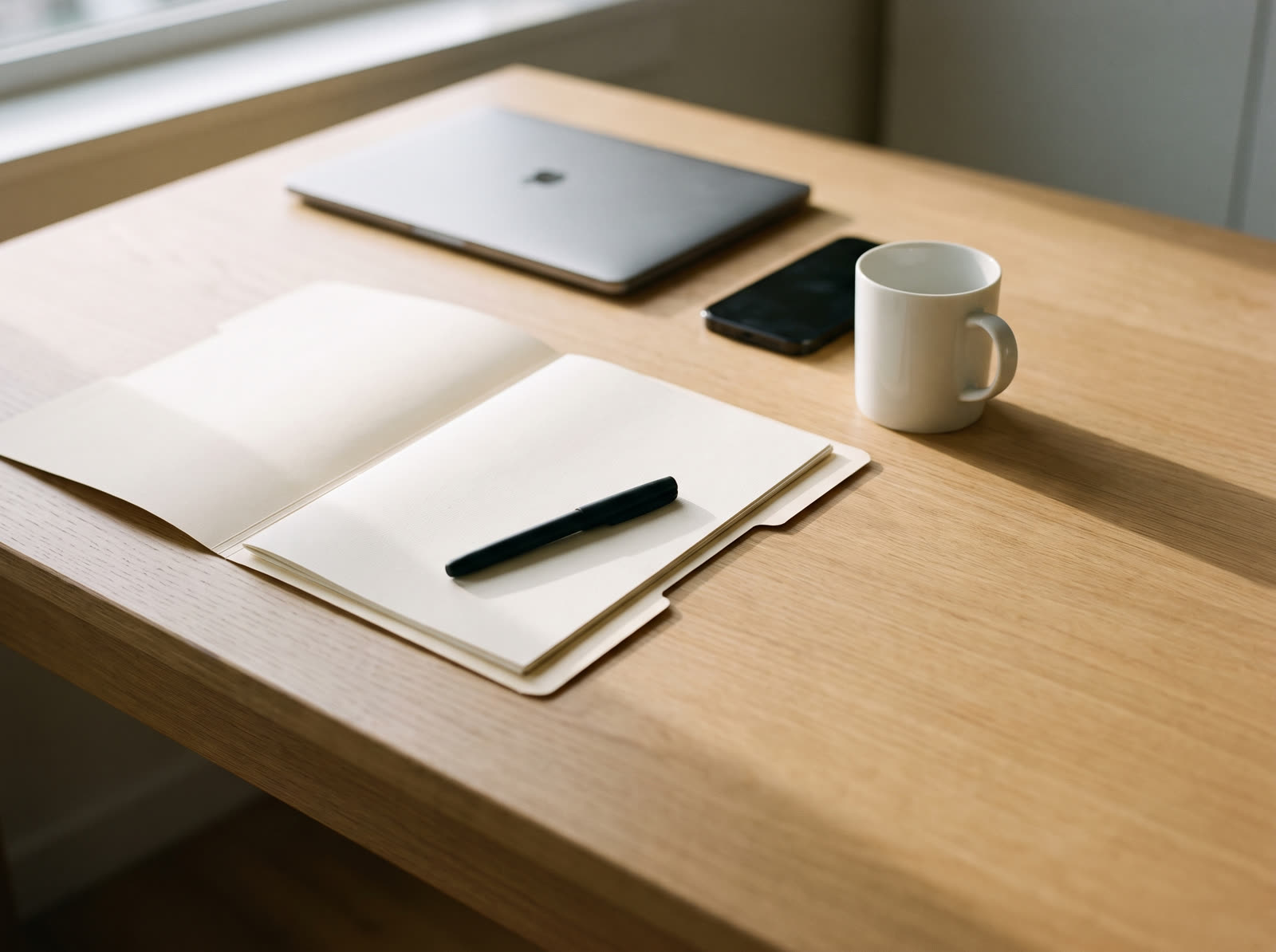 A tidy desk with a closed laptop, an open paper folder and a pen